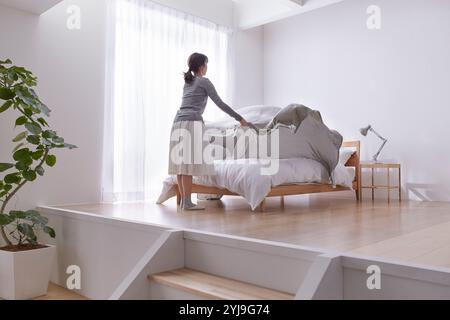 Frau, die das Bett in einem einfachen Schlafzimmer mit Treppenstufen herstellt Stockfoto