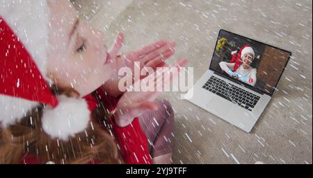 Bild von Schnee, der über eine lächelnde Frau mit weihnachtsmann fällt, während eines Videogesprächs mit ihrer Familie. weihnachten, Tradition und Festkonzept digital gen Stockfoto