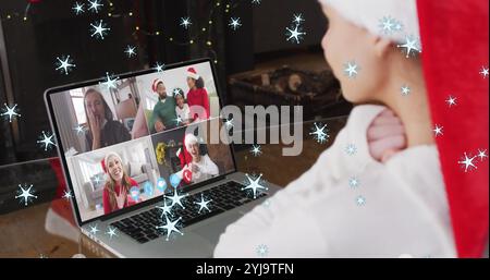 Bild von Schnee, der über eine lächelnde Frau mit weihnachtsmann fällt, während eines Videogesprächs mit ihrer Familie. weihnachten, Tradition und Festkonzept digital gen Stockfoto