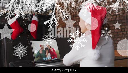 Bild von Schnee, der über eine lächelnde Frau mit weihnachtsmann fällt, während eines Videogesprächs mit ihrer Familie. weihnachten, Tradition und Festkonzept digital gen Stockfoto