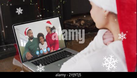 Bild von Schnee, der über eine lächelnde Frau mit weihnachtsmann fällt, während eines Videogesprächs mit ihrer Familie. weihnachten, Tradition und Festkonzept digital gen Stockfoto