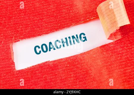 Geschäftskonzept. Der Satz, Text, Wortwahl COACHING ist auf weißem Papier unter rot gerissenem Papier geschrieben. Stockfoto