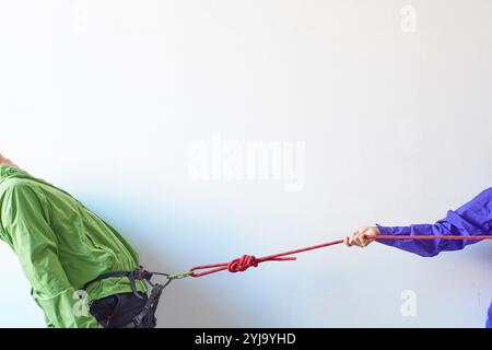 Kletterer wird von einem Gurtzeug mit Karabiner vor einer weißen Wand gezogen Stockfoto