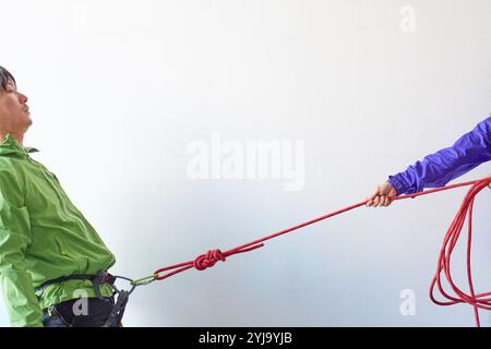 Kletterer wird von einem Gurtzeug mit Karabiner vor einer weißen Wand gezogen Stockfoto