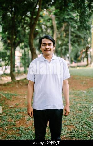 Ein südostasiatischer Mann, der auf einem offenen Grasfeld auf einem Stadtplatz steht und einen Moment der Ruhe und des Raumes festnimmt. Ideal für Projekte, die sich auf städtisches Leben konzentrieren, Stockfoto