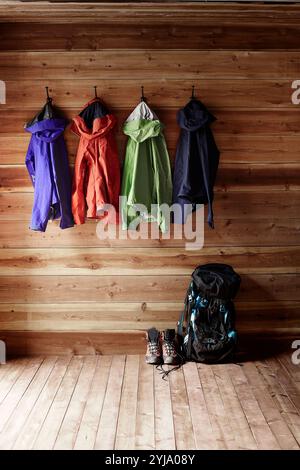 Vier Paar Bergsteigerbekleidung in vier verschiedenen Farben, die an Haken in der Hütte hängen, Schuhe und Rucksack auf dem Boden Stockfoto