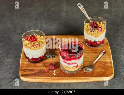 Eine Nahaufnahme dreischichtiger Beerenparfaits in Gläsern mit leuchtenden Beeren, cremigen Schlagablagen und bröckeligen Keksgrundlagen. Stockfoto