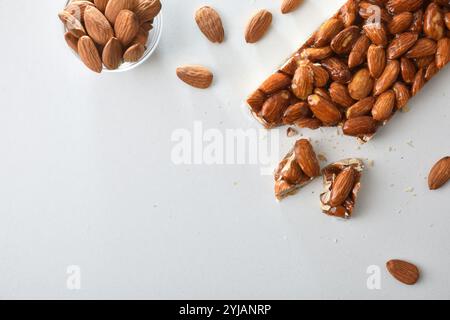 Nougat Bar mit ganzen Mandeln und Honig bedeckt mit Karamell und Schüssel mit natürlichen Mandeln isoliert auf weißem Tisch. Draufsicht. Stockfoto