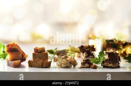 Auswahl an weihnachtlichen Nougats mit verschiedenen Geschmacksrichtungen stapelbar in Portionen hintereinander auf einem weißen Tisch mit weihnachtlicher Dekoration und Atmosphäre. Vorderansicht Stockfoto