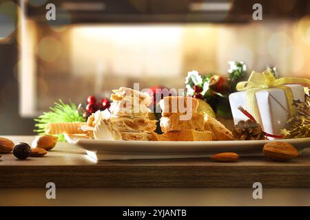 Teller mit frisch zubereiteten Nougatstücken auf einem Holztisch mit Weihnachtsdekoration und dunklem Küchenhintergrund mit warmer Beleuchtung. Vorderansicht. Stockfoto