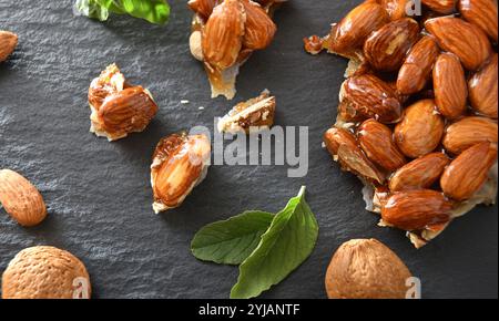 Harter Nougat mit ganzen und gehackten Mandeln auf einem Schieferteller mit natürlichen Mandeln und Blättern aus nächster Nähe. Draufsicht. Stockfoto