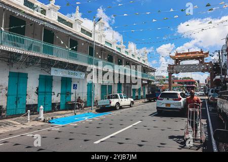 Eine belebte Straße in Port Louis City, Mauritius, voll mit Autos, die am Straßenrand geparkt sind, umgeben von Gebäuden und einer Moschee. Stockfoto