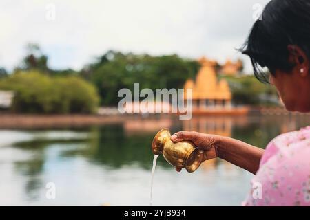 Eine Frau gießt im Kontext der hinduistischen religiösen Traditionen auf Mauritius Wasser aus einem Messinghahn als Teil eines bedeutenden Rituals. Stockfoto