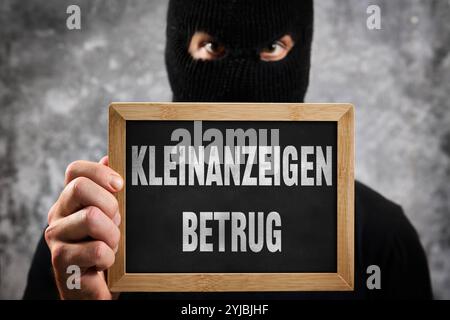 Bayern, Deutschland - 14. November 2024: Kleinanzeigen-Betrug, geschrieben auf einem Schild vor einer maskierten anonymen / unbekannten Person. Symbolisches Image für Betrug im Internet durch Werbung und Anzeigen wie Ebay Kleinanzeigen. FOTOMONTAGE *** Kleinanzeigen Betrug, stehen auf einem Schild vor maskierter anonymer / unbekannter Person. Symbolbild für Betrug im Internet über Inserate und Anzeigen wie Ebay Kleinanzeigen. FOTOMONTAGE Stockfoto