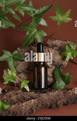 Einfache Flasche Mit Ätherischem Öl. Kosmetisch. Natürliches Öl, grüne Blätter auf braunem natürlichem Holz, Efeu, Baumrinde. Hintergrund. Podiumshintergrund für Pro Stockfoto