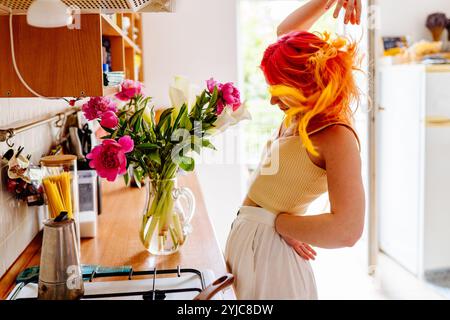 Junge Frau tanzt fröhlich in einer hellen Küche mit Blumen Stockfoto