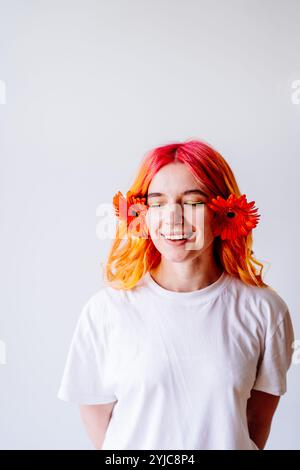 Lächelnde junge Frau mit rosa Haaren und orangen Blumen Stockfoto