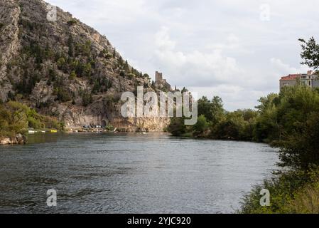 Blick auf die Stadt Omis vom Fluss Cetina, Kroatien, mit dem malerischen Fluss, der durch das Tal fließt, umgeben von zerklüfteten Bergen und dem Saibling der Stadt Stockfoto