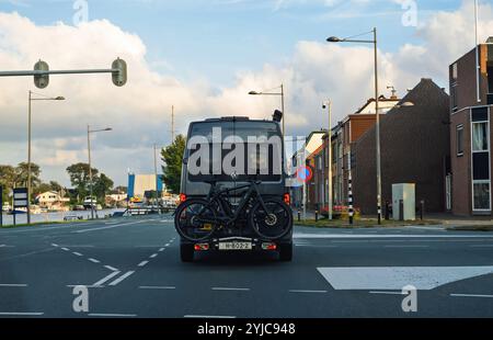 Texel, Niederlande - 29. August 2024: Ein Volkswagen Wohnmobil mit zwei hinten montierten Fahrrädern wird durch eine niederländische Stadt mit einem malerischen Kanal und Gebäuden im Hintergrund gefahren Stockfoto