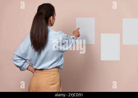 Selbstbewusste, hübsche Geschäftsfrau, die auf klebenden Papieren an der Wand, Rückansicht, Mock-up, Projekt- und Terminkonzept zeigt Stockfoto