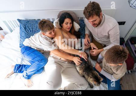 Familie der schwangeren Mutter, Vater, zwei Kinder und ihre Katze im Bett im Schlafzimmer Stockfoto