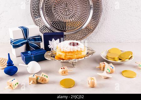 Festliche Donuts auf einer Silberplatte zwischen den Schachteln mit Geschenken für den Hanukka-Feiertag. Dreidels aus Holz mit Tetraeder. Das Konzept von Hanukka Stockfoto