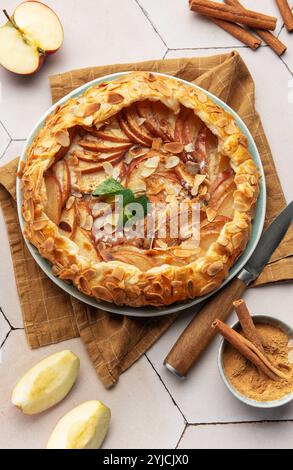 Frisch gebackene Apfelgalette, dekoriert mit Mandelblättern, Zimtstangen und Minzblättern, auf einem weiß gekachelten Tisch Stockfoto