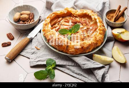 Frisch gebackene Apfelgalette, dekoriert mit Mandelflocken, Minzblättern, Zimt und Pekannüssen, serviert auf Keramikplatte Stockfoto