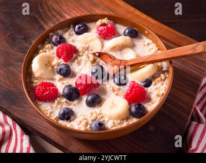 Gesunde Haferflocken aus Stahl mit Banane, Heidelbeeren, Himbeeren mit Mandelmilch in einer braunen Schüssel Stockfoto