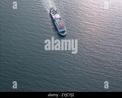 Die Fähre bewegt sich stetig über ruhiges Wasser und hinterlässt während des sonnigen Mittags sanfte Wellen. Stockfoto