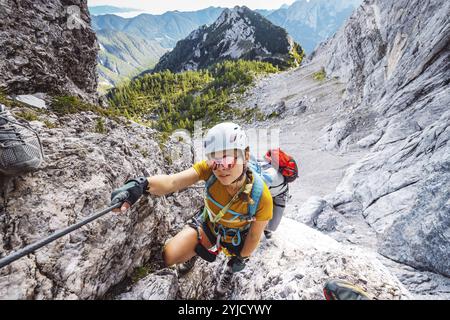 Eine weiße Bergsteigerin, die den Berg auf dem Klettersteig hoch oben in den Berggipfeln hinaufklettert. Frau, die eine Schutzausrüstung trägt und benutzt Stockfoto