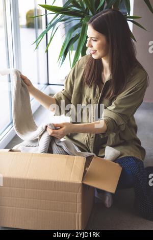 Junge kaukasische Frau erhält eine große Kiste mit ihren Online-Bestellungen. Frau, die das Paket öffnet und begeistert ist, das Zeug zu sehen, das sie gekauft hat. Stockfoto