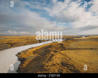 Leuchtend blauer Fluss, der an einem kalten Tag im Herbst unter einer Brücke durch das isländische Festland fließt. Stockfoto