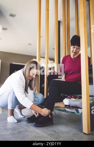 Junge kaukasische Frau, Krankenschwester, bei einem Hausbesuch, um eine Seniorin zu versorgen. Die Schwester hilft einer Seniorin bei den täglichen Aufgaben, hilft ihr, zu laufen Stockfoto
