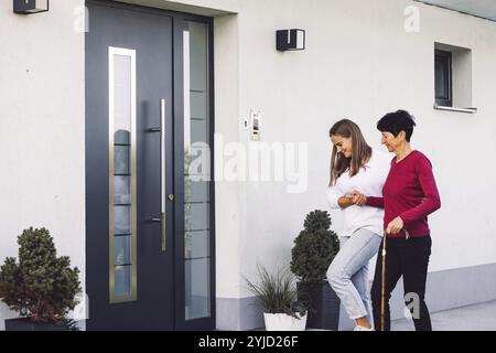Junge kaukasische Frau, Krankenschwester, bei einem Hausbesuch, um eine Seniorin zu versorgen. Die Schwester hilft einer Seniorin bei den täglichen Aufgaben, hilft ihr, zu laufen Stockfoto