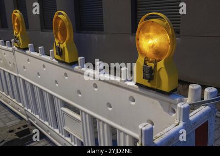 Blinkende gelbe Rundlichter an weißer Straßensperre bei Nacht, um eine Baustelle zu schützen und den Verkehr abzulenken Stockfoto