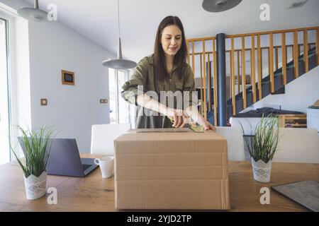 Junge kaukasische Frau erhält eine große Kiste mit ihren Online-Bestellungen. Frau, die das Paket öffnet und begeistert ist, das Zeug zu sehen, das sie gekauft hat. Stockfoto