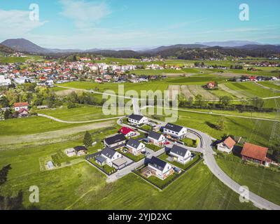 Luftaufnahme, Drohne fliegt über Vorstadtgemeinde auf dem Land. Einfamilienhäuser in den Vororten umgeben von Wald und grünen Feldern Stockfoto