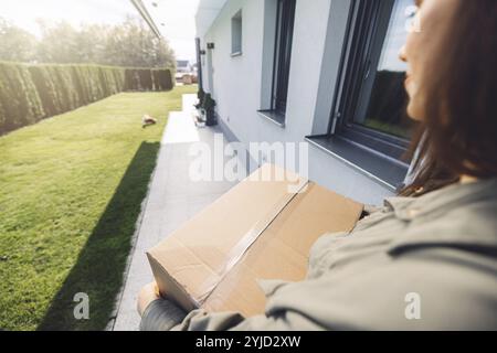 Junge kaukasische Frau erhält eine große Kiste mit ihren Online-Bestellungen. Frau, die das Paket öffnet und begeistert ist, das Zeug zu sehen, das sie gekauft hat. Stockfoto