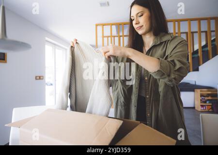 Junge kaukasische Frau erhält eine große Kiste mit ihren Online-Bestellungen. Frau, die das Paket öffnet und begeistert ist, das Zeug zu sehen, das sie gekauft hat. Stockfoto