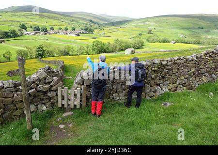 Zwei Männer (Wanderer) stehen an einem Tor und einer trockenen Steinmauer, die über Hay Meadows nach Thwaite in Swaledale am Pennine Way, Yorkshire Dales, England zeigt. Stockfoto