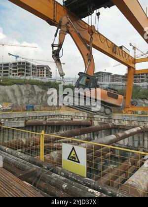 Kranhub eines Baggers auf einer Baustelle mit sichtbaren Gebäuden in der Nähe Stockfoto