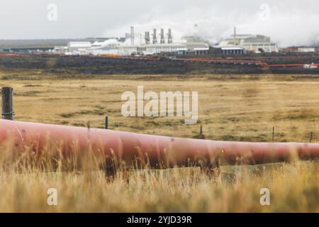 Geothermiekraftwerk, Warmwasserkraftwerk in Island. Dampf, der aus den Schornsteinen der Anlage herausgerollt wird, rote große Rohre, die über das Gelände laufen, gefüllt Stockfoto