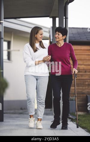 Junge kaukasische Frau, Krankenschwester, bei einem Hausbesuch, um eine Seniorin zu versorgen. Die Schwester hilft einer Seniorin bei den täglichen Aufgaben, hilft ihr, zu laufen Stockfoto