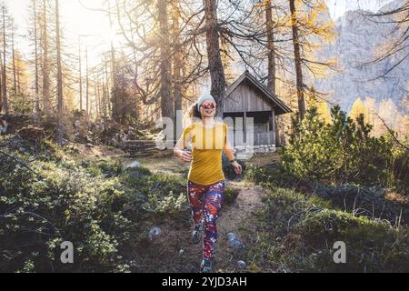 Fröhliche Wanderer, die im Herbstwald läuft, trägt ein orangenes Hemd und bunte Leggings. Eine Frau, die in die Luft springt, während sie durch die Fores wandert Stockfoto