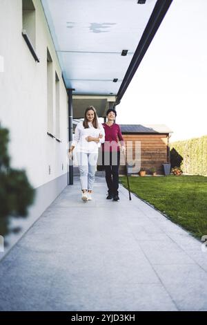 Junge kaukasische Frau, Krankenschwester, bei einem Hausbesuch, um eine Seniorin zu versorgen. Die Schwester hilft einer Seniorin bei den täglichen Aufgaben, hilft ihr, zu laufen Stockfoto
