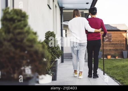 Junge kaukasische Frau, Krankenschwester, bei einem Hausbesuch, um eine Seniorin zu versorgen. Die Schwester hilft einer Seniorin bei den täglichen Aufgaben, hilft ihr, zu laufen Stockfoto