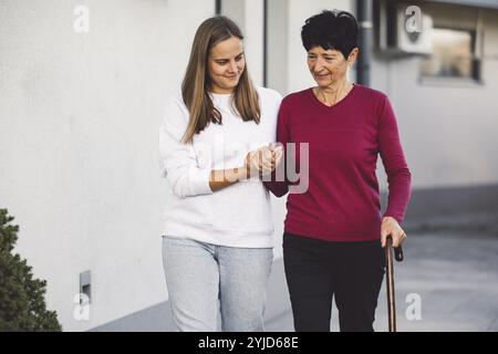 Junge kaukasische Frau, Krankenschwester, bei einem Hausbesuch, um eine Seniorin zu versorgen. Die Schwester hilft einer Seniorin bei den täglichen Aufgaben, hilft ihr, zu laufen Stockfoto
