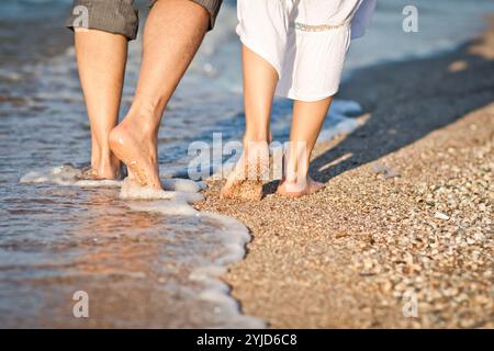 Barfuß laufen. Mann und Frau gehen am Ufer entlang und hinterlassen Spuren. Frauen- und Herrenfüße am Ufer eines Sandstrandes an einem sonnigen Tag. Stockfoto