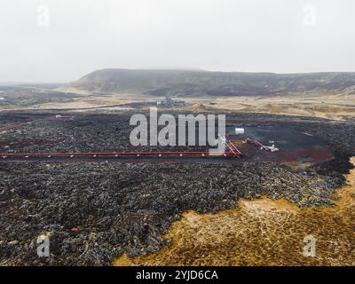 Geothermiekraftwerk, Warmwasserkraftwerk in Island. Dampf, der aus den Schornsteinen der Anlage herausgerollt wird, rote große Rohre, die über das Gelände laufen, gefüllt Stockfoto